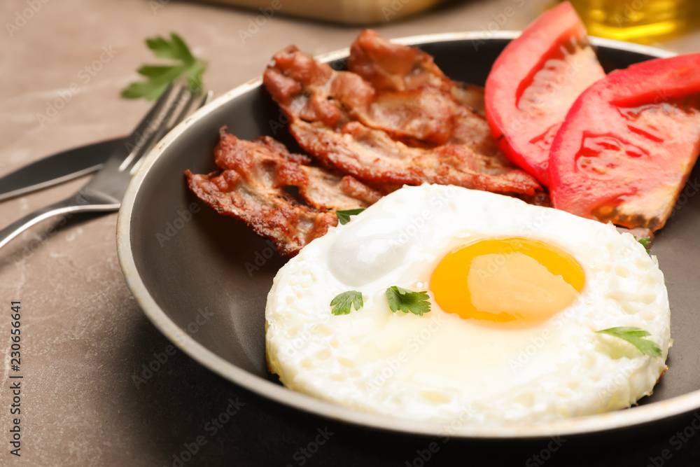 Pan with fried sunny side up egg, bacon and tomato on table, closeup Pan with fried sunny side up egg, bacon and tomato on table, closeup