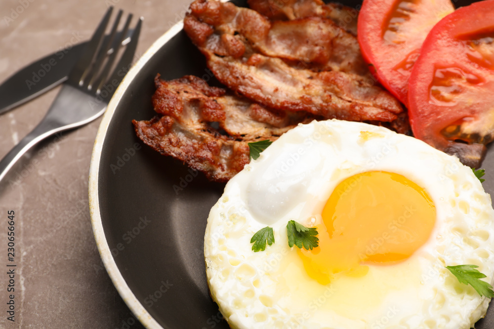 Pan with fried sunny side up egg, bacon and tomato on table, closeup Pan with fried sunny side up egg, bacon and tomato on table, closeup