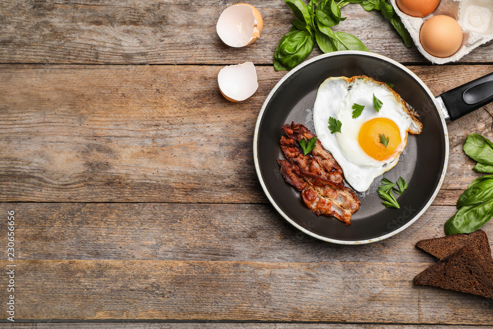 Fried sunny side up egg with bacon in pan on wooden background, flat lay. Space for text Fried sunny side up egg with bacon in pan on wooden background, flat lay. Space for text