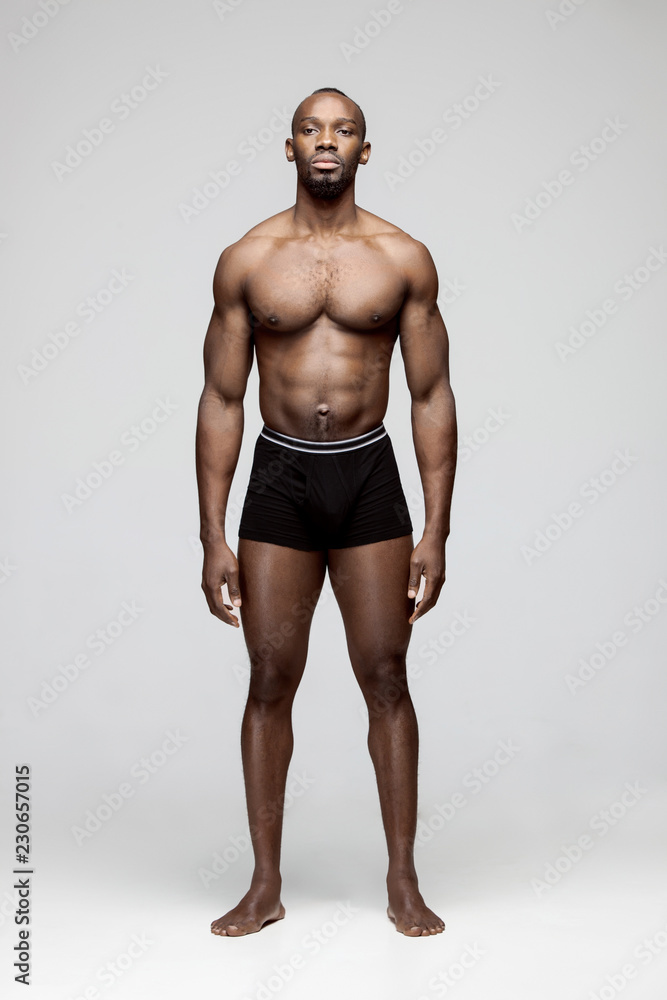Fit young man with beautiful torso, isolated on gray background. The naked torso of African American man posing at studio. The muscular body, fitness, sports, healthy lifestyle and bodybuilder concept