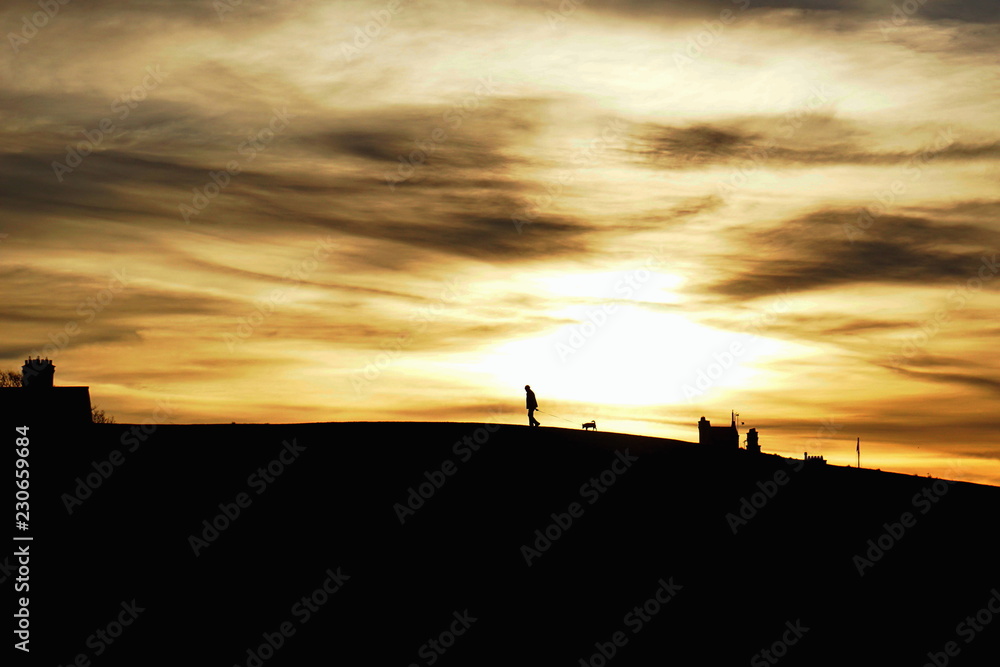 Fototapeta premium The walk. Silhouettes of an old man and his dog against dramatic sunset