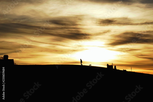 The walk. Silhouettes of an old man and his dog against dramatic sunset