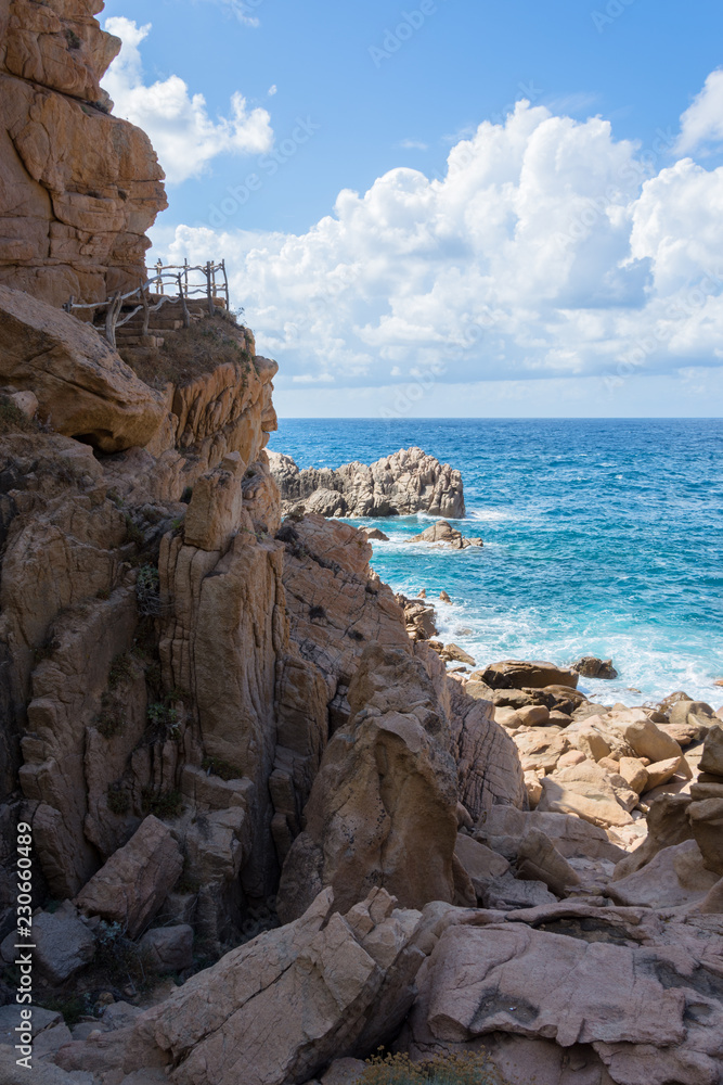 Costa rocciosa con mare in vista, poche nuvole, bella giornata di sole e sentiero nella roccia