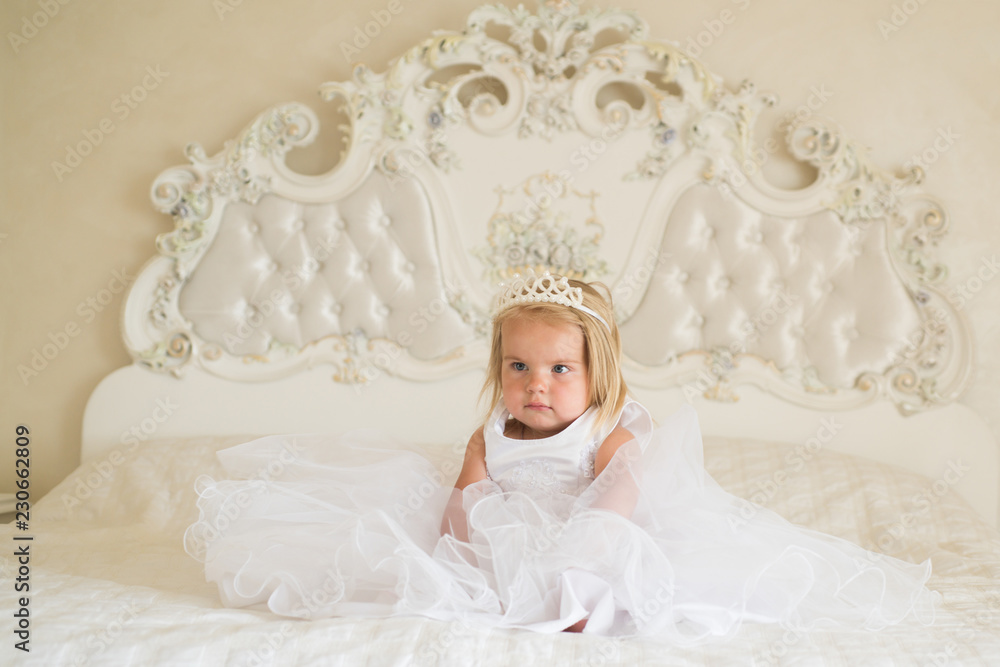 Real princess. Hair accessory. Little girl wear crown and hairstyle. Little  child with long blond hair. Small blond child sit on bed. Beautiful  hairstyles for baby girls. Her beauty shines through Stock