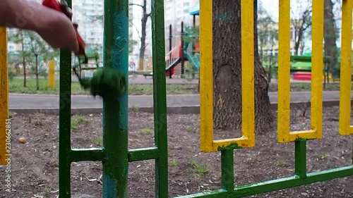 A worker paint green roller painting a yellow-green fence on the background playground