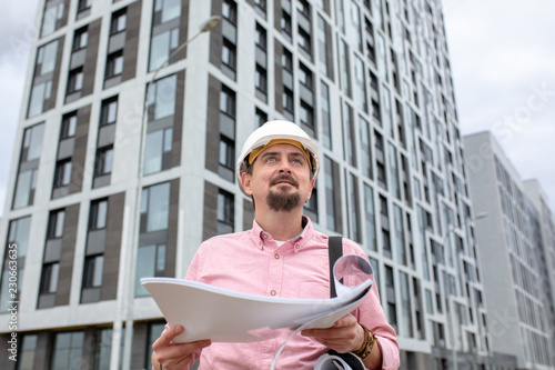 Portrait of architect at work with helmet in a construction site, reads the plan, paper projects