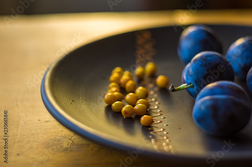 still life - juicy blue plums and sea buckthorn berries in a ceramic plate on a wooden background