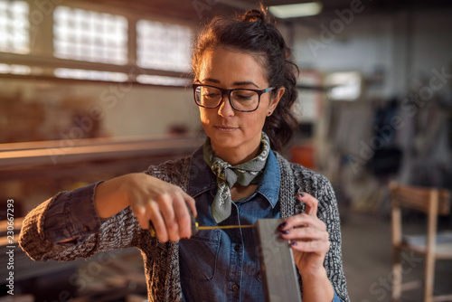 Young female industrial engineer taking measures of metal pipe in her workshop.