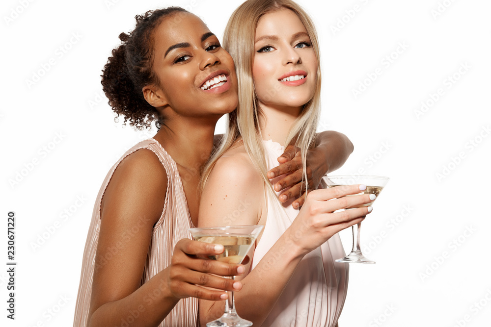 Portrait of good-looking young women in elegant evening dresses with champagne glasses. Cheerful lovely girls posing at studio. Isolated on white background Portrait of good-looking young women in elegant evening dresses with champagne glasses. Cheerful lovely girls posing at studio. Isolated on white background
