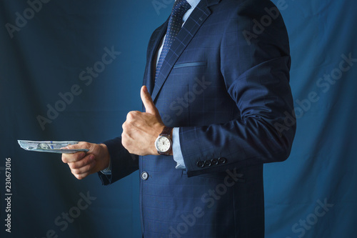 A man in a suit transfers money and holds his thumb up, side view.