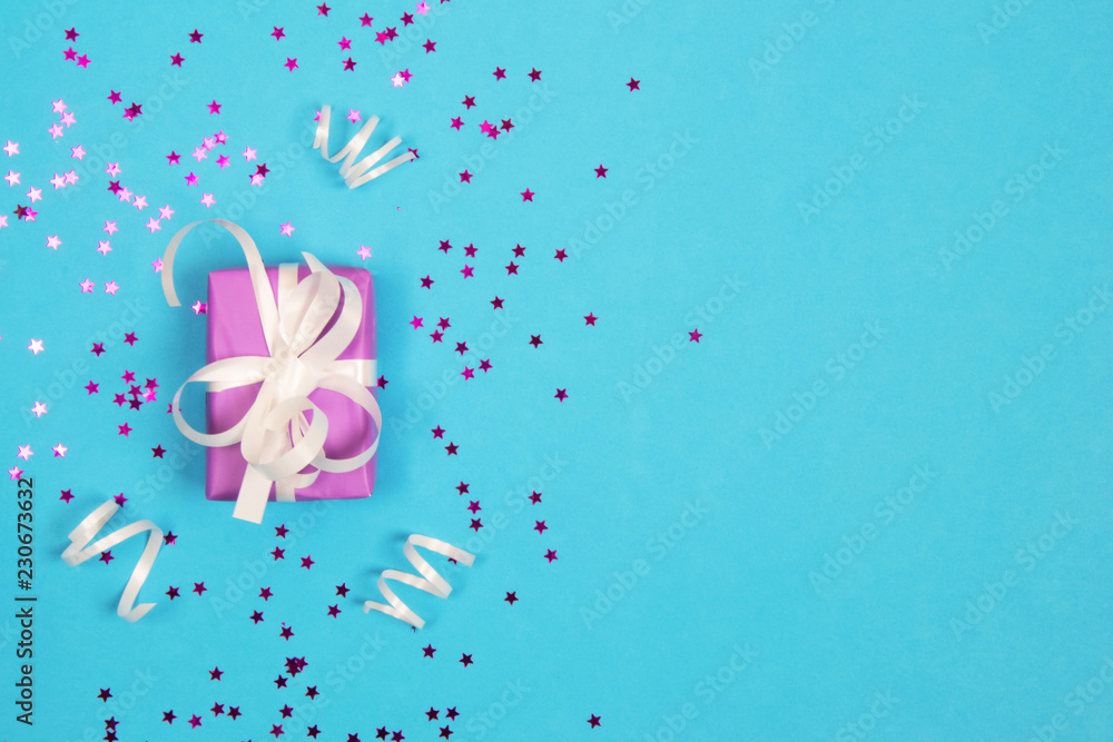 A gift box in purple wrapping paper, tied with white ribbons and decorated with a white bow, on a blue background, along with a pink one.