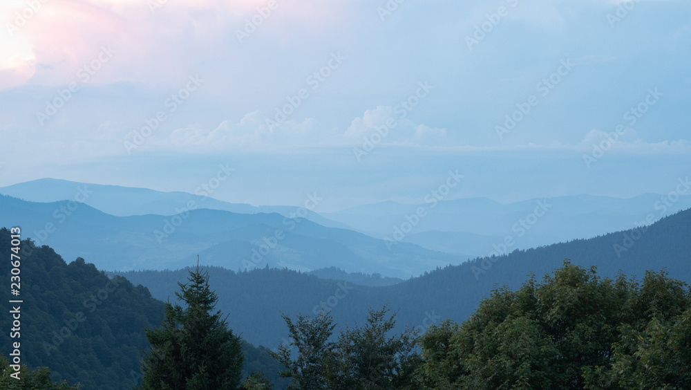 Shank of the evening in Carpathians mountains at summer, west Ukraine. Ukrainian nature panoramic landscape. Hillsides covered with dense forest. Dark ranges under evening sky. Blurred background Shank of the evening in Carpathians mountains at summer, west Ukraine. Ukrainian nature panoramic landscape. Hillsides covered with dense forest. Dark ranges under evening sky. Blurred background