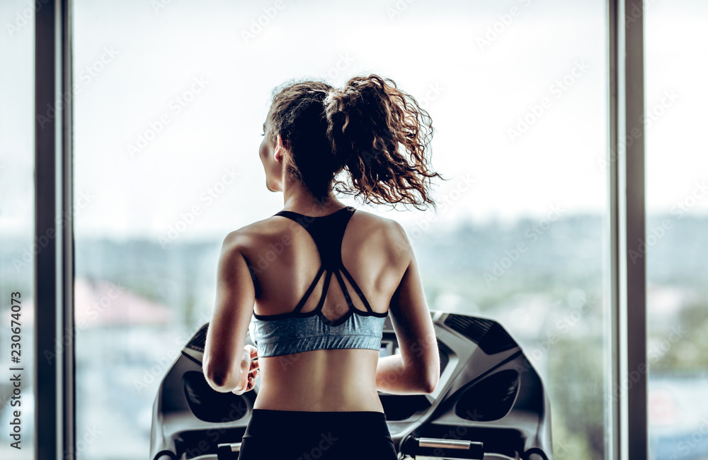 Fototapeta Atrakcyjna kobieta działa na bieżni w siłowni sportu, życia sportowego i sprzętu sportowego. Widok z tyłu.