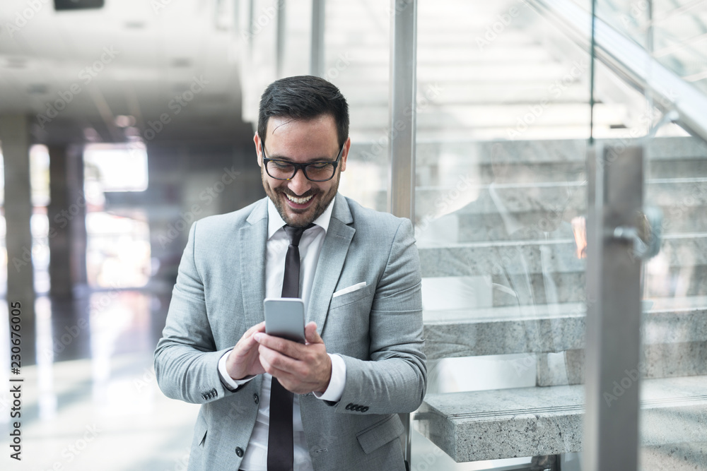 Happy young businessman using smart phone for texting while leaning on the glass. Happy young businessman using smart phone for texting while leaning on the glass.