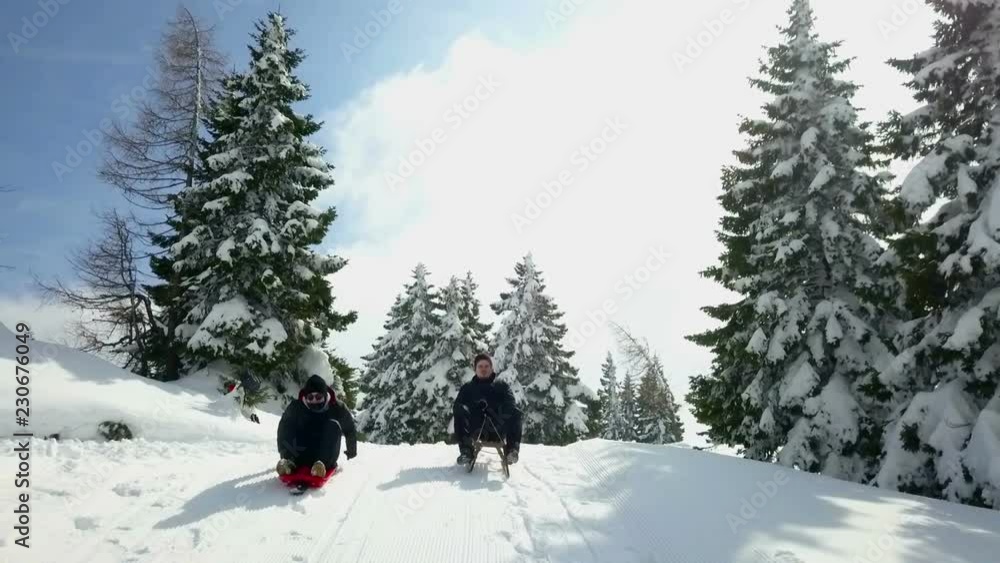 Two guys are sledding down the hill on a nice winter day. They're having fun spending some time outdoors. Two guys are sledding down the hill on a nice winter day. They're having fun spending some time outdoors.