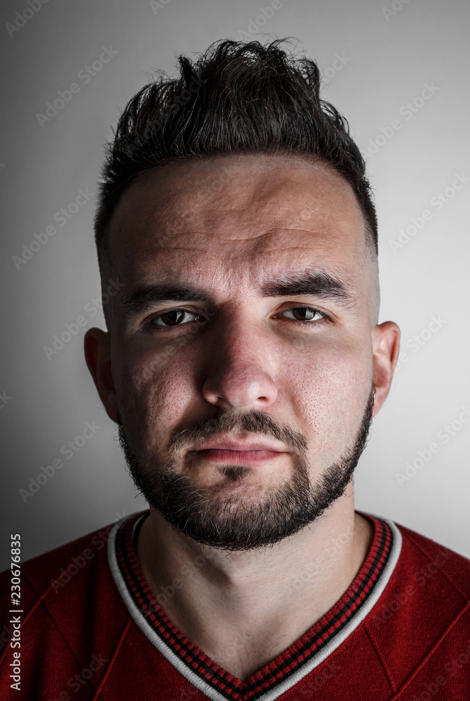 Obraz premium Close up portrait of young handsome male with beard and trendy hairdo, with serious face expression on gray background