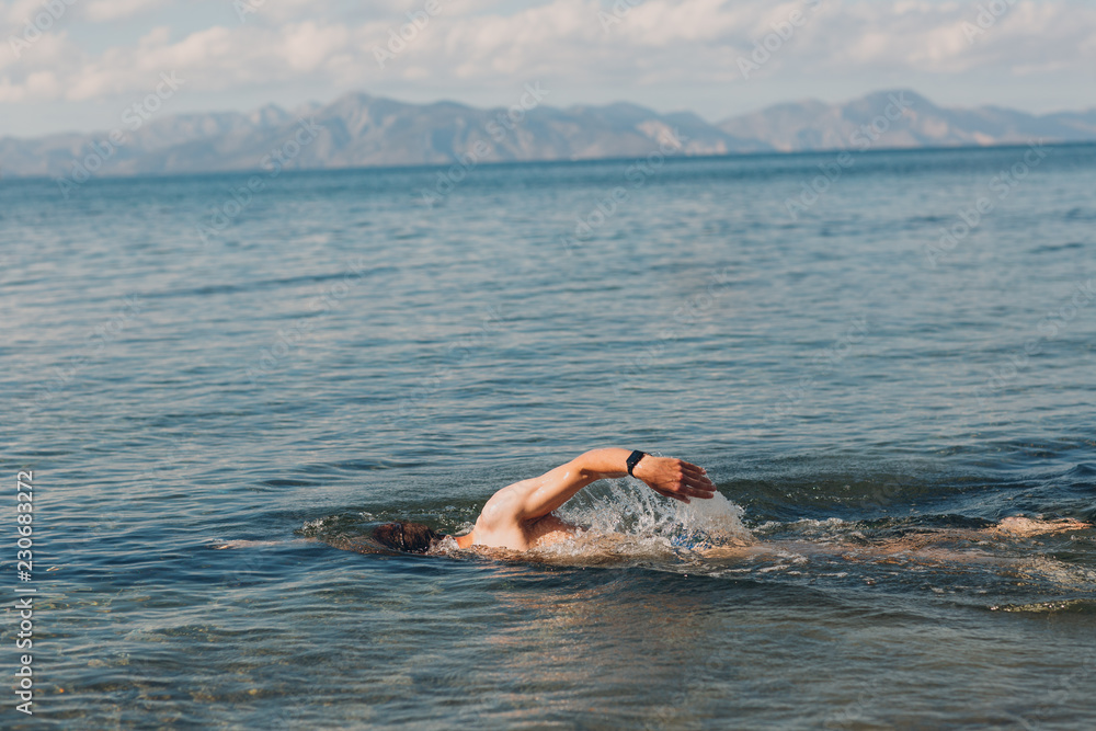 A young man swims in the sea against the backdrop of mountains