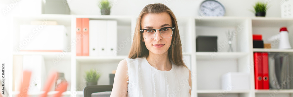 Beautiful young girl is sitting at the table in the office, holding a pen in her hand and filling out the documents. Beautiful young girl is sitting at the table in the office, holding a pen in her hand and filling out the documents.