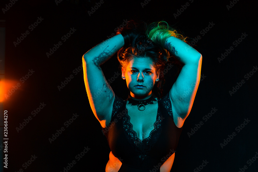 Close up portrait of curvy alternative model with colored hair and lace bodysuit and fishnets under blue and orange lighting Close up portrait of curvy alternative model with colored hair and lace bodysuit and fishnets under blue and orange lighting