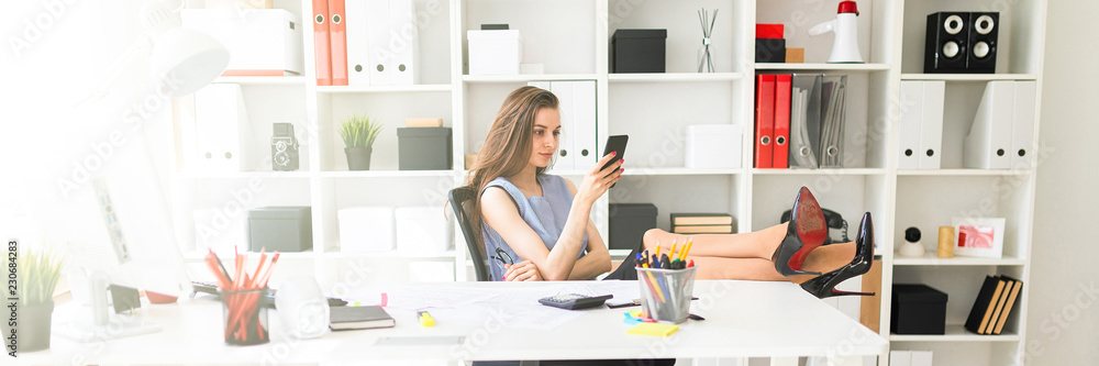A beautiful young girl in the office has put her feet on the table and is holding glasses and a phone. A beautiful young girl in the office has put her feet on the table and is holding glasses and a phone.