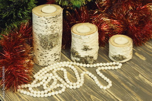 Birch candlesticks and beads made of artificial pearls, red and green knick-knackery. Gray wooden background.
