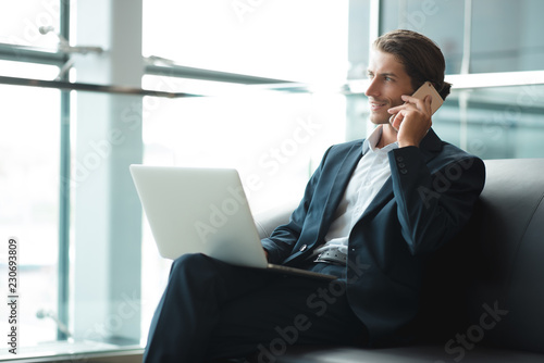 Young handsome student typing on his notebook his diploma. Student discussing on the phone universitie's timetable. Education online. Work on freelance. Software development. 