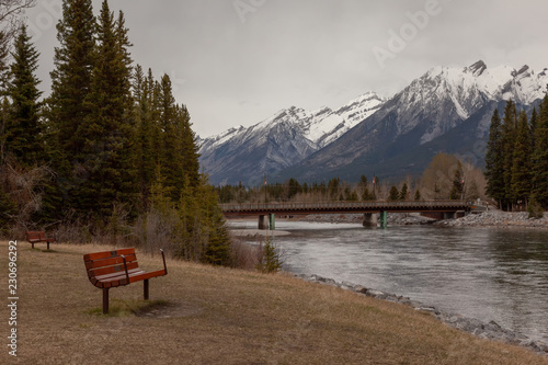 Sitting bench on the bow riverbank view of the Bow River, the snow capped mountain and bridge to downtown Canmore in the Canadian Rockies in Alberta