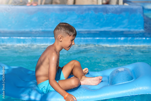 Portrait of happy Caucasian boy having fun with inflatable mattress in swimming pool at resort. Side view.