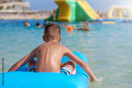 Portrait of happy Caucasian boy having fun with inflatable mattress in swimming pool at resort. Back view.