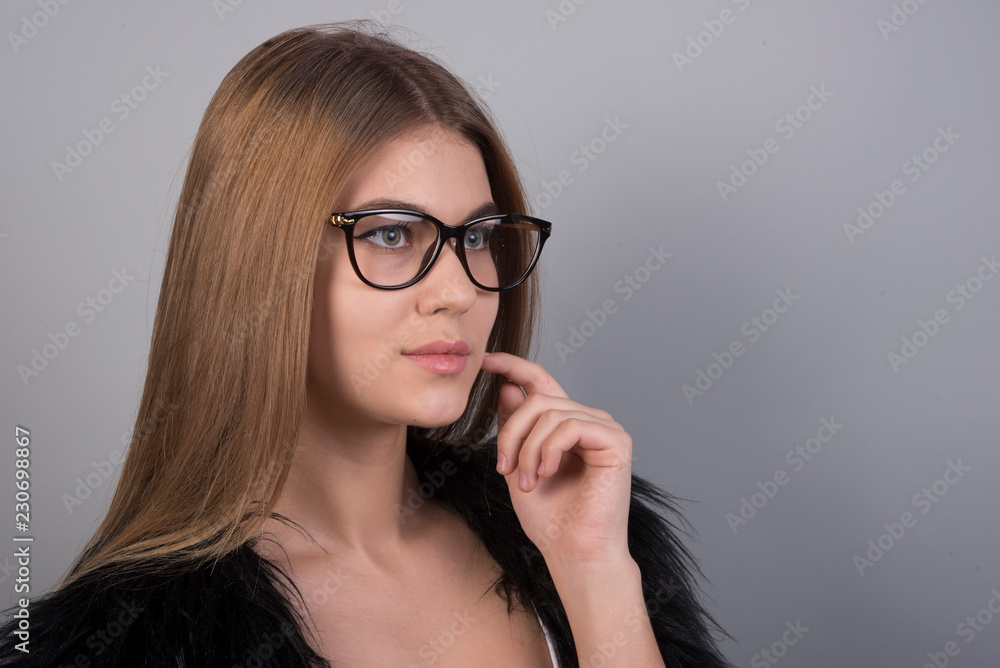 Young beautiful girl with glasses standing in front of grey background and looking forward, a lot of clean space Young beautiful girl with glasses standing in front of grey background and looking forward, a lot of clean space