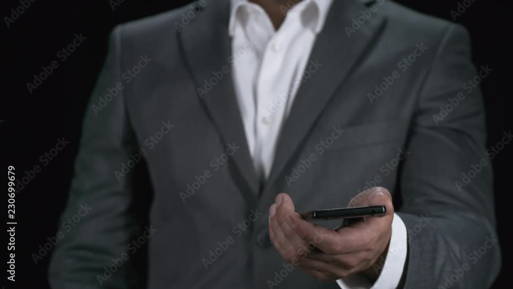 Unrecognizable man standing isolated on black background and holding mobile phone, then tapping on touchscreen to turn on invisible holographic interface. Footage suitable for adding AR elements Unrecognizable man standing isolated on black background and holding mobile phone, then tapping on touchscreen to turn on invisible holographic interface. Footage suitable for adding AR elements