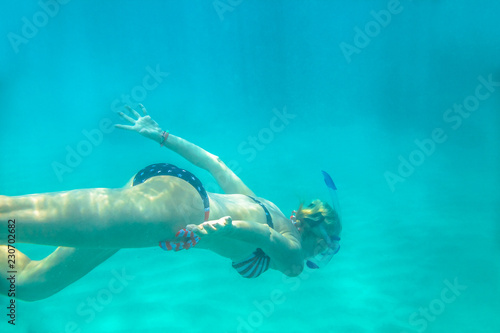 Female in apnea swims underwater with american flag bikini. Underwater background of a woman snorkeling and doing skin diving. Watersport activity in Hawaii. Tropical destination holiday concept.