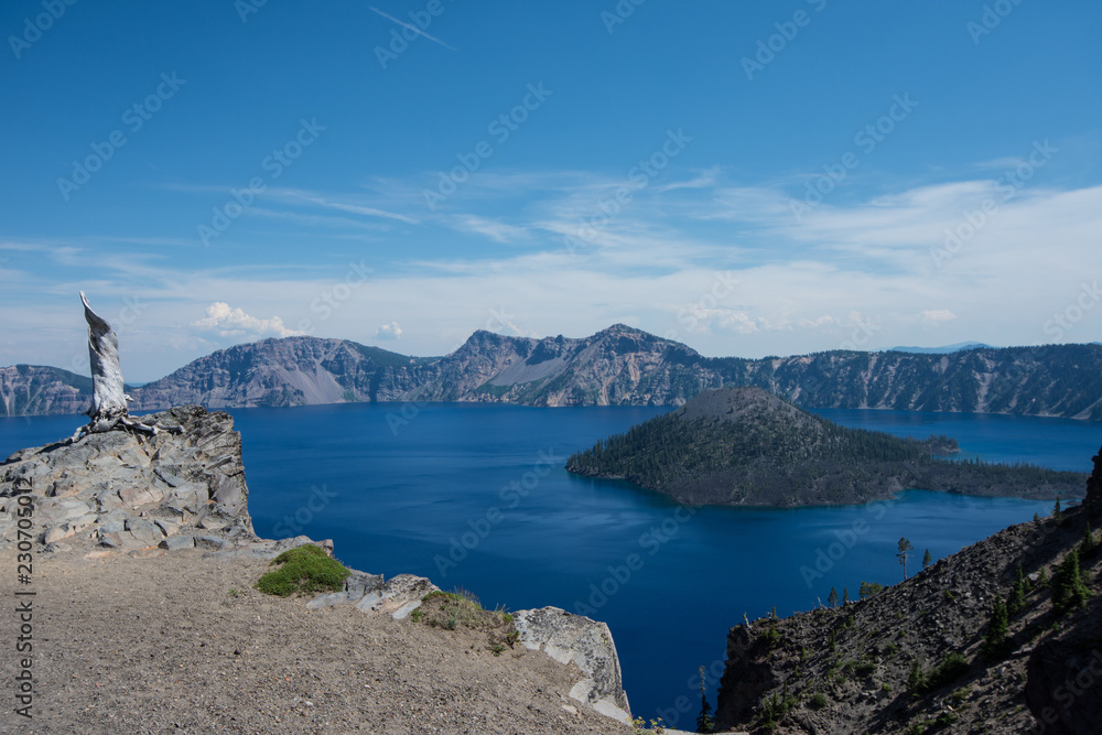 Wide angle view of Crater Lake National Park in Oregon, on sunny clear summer day. Wizard Island and tree stump in photo