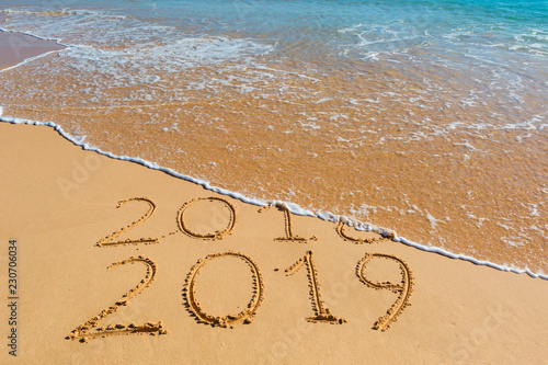 2018 2019 inscription written in the wet yellow beach sand being washed with sea water wave