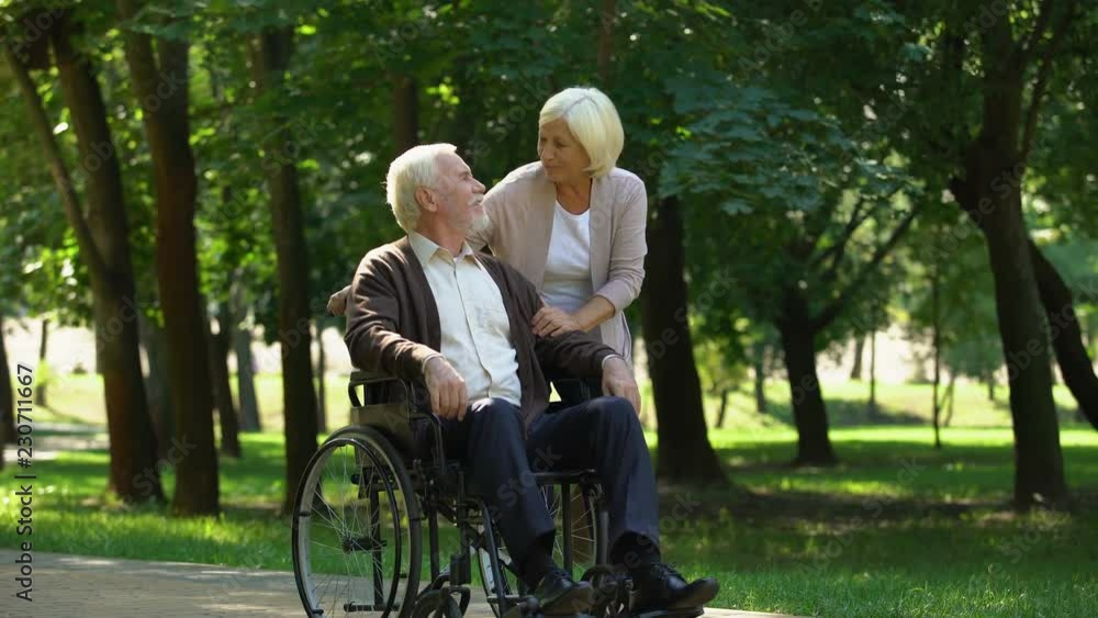 Adult couple walking in park, wife kissing her disabled husband, rehabilitation Adult couple walking in park, wife kissing her disabled husband, rehabilitation