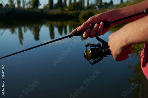 The lake is a bright . A fisherman on the bank. Fishing rod wheel closeup. Spinning reel. The concept of outdoor activities. Tackles for pike, perch, zander.