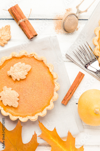 Pumpkin pie with cinnamon and cookies on gray napkins on white wooden background with autumn yellow leaves.