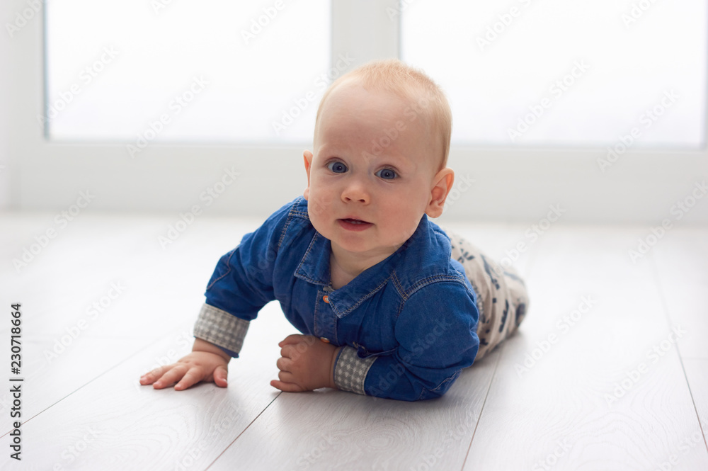 Portrait of a cute little baby in blue denim shirt laying on the floor. Candid image of young baby playing at home/Little baby play on the floor Portrait of a cute little baby in blue denim shirt laying on the floor. Candid image of young baby playing at home/Little baby play on the floor