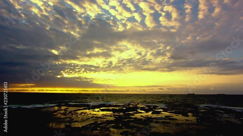 Timelapse footage of a sunrise overlooking a water ladden rock ledge. A sinlge fishermen can be seen in bottom right of frame. Two large ships can be seen on horizon. Located Redhead, NSW, Australia. photo