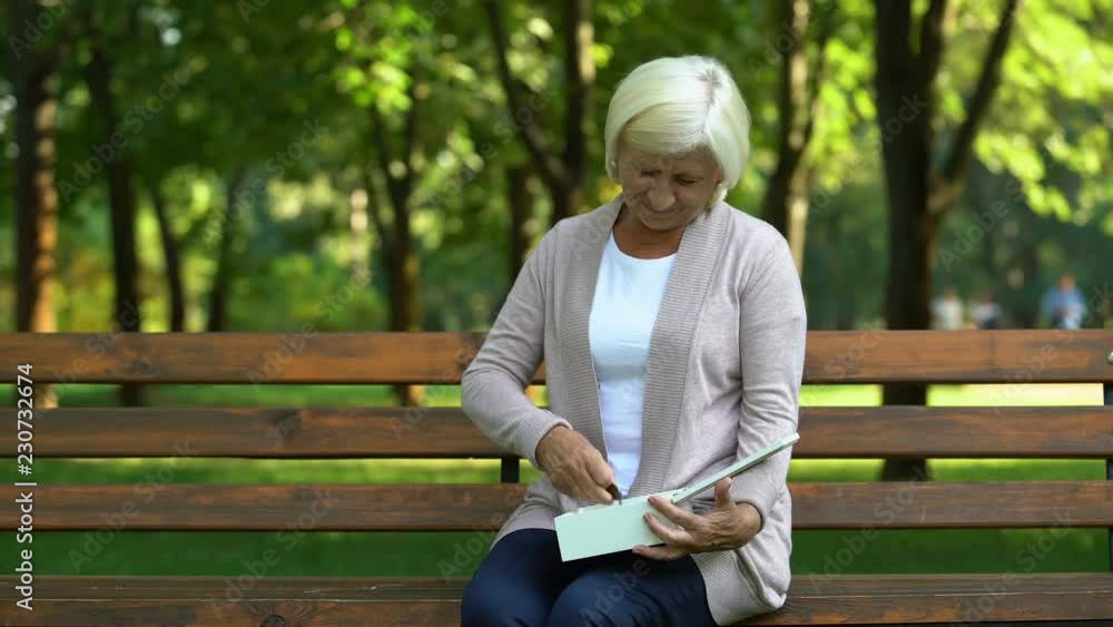 Old lady sitting on bench looking at pendant, remembering her husband, loss Old lady sitting on bench looking at pendant, remembering her husband, loss