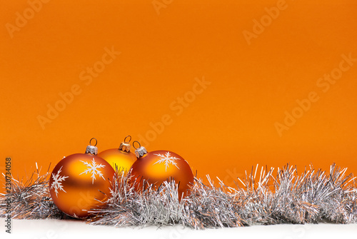 Three orange bauble Christmas decorations against an orange background with space for adding text.