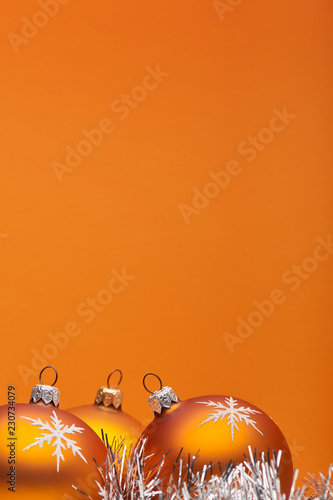 Three orange bauble Christmas decorations close up against an orange background with space for adding text vertical.