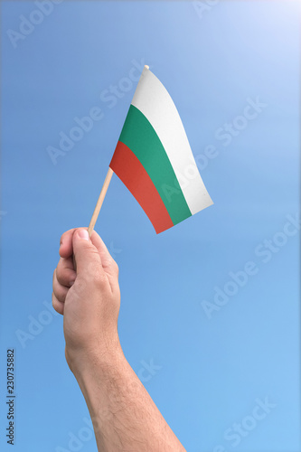 Hand holding Bulgeria flag high in the air, with a clear blue sky photo