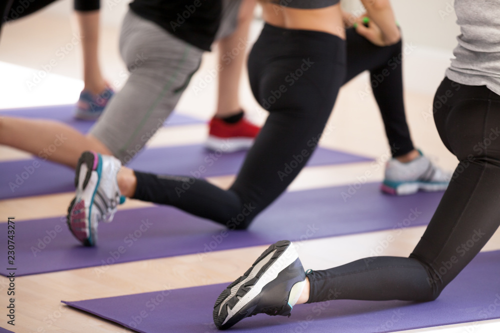 Slim people wearing sportswear and sneakers doing lunge standing on rubber  carpet mat, close up humans