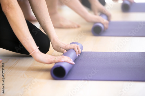 Fototapeta Naklejka Na Ścianę i Meble -  Close up hands of girls and guys unrolling mats human preparing for fitness workout at gym centre studio. Sportive athletic people after yoga class folding rubber carpets and finishing sport training
