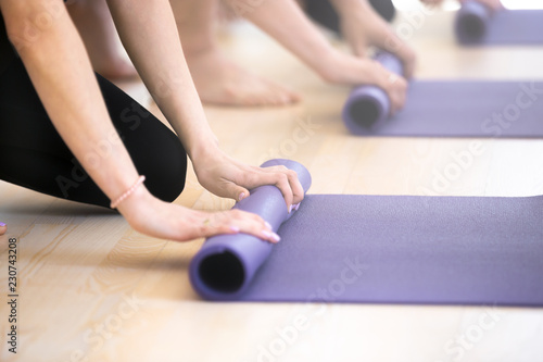 Close up hands of girls and guys unrolling mats human preparing for fitness workout at gym centre studio. Sportive athletic people after yoga class folding rubber carpets and finishing sport training photo