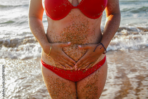 Women in red bikini with her hands on belly with sea waves on background