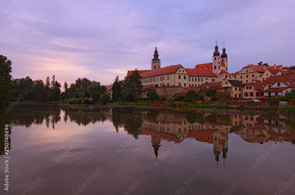 Panoramic view of Telc castle, pond with park, Name of Jesus Church and tower of the Church of St. Jakub. Buildings are reflected in the water. Early morning landscape. A UNESCO World Heritage Site