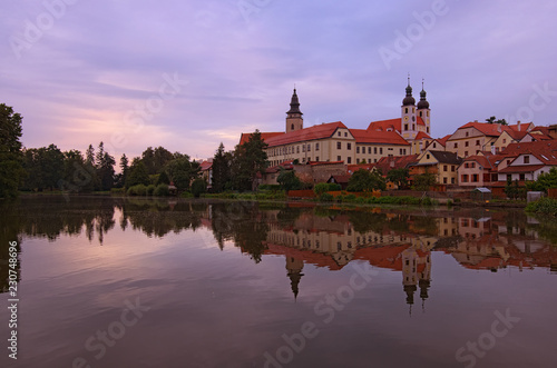 Panoramic view of Telc castle, pond with park, Name of Jesus Church and tower of the Church of St. Jakub. Buildings are reflected in the water. Early morning landscape. A UNESCO World Heritage Site