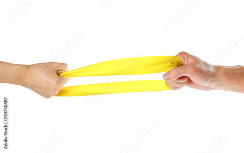 The hands pull yellow athletic elastic band in different directions. Close up. Isolated on white background